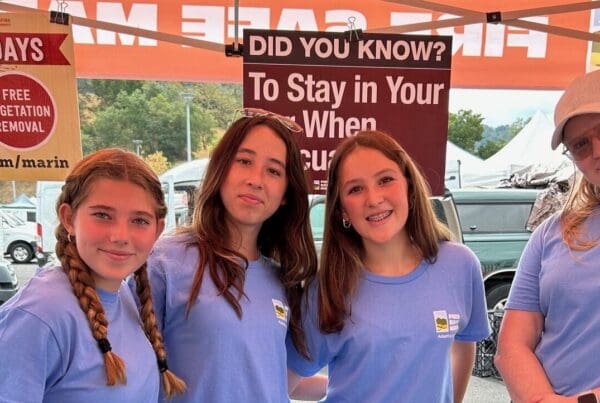 High school students volunteering at farmers market, standing at a booth for fire safety program.
