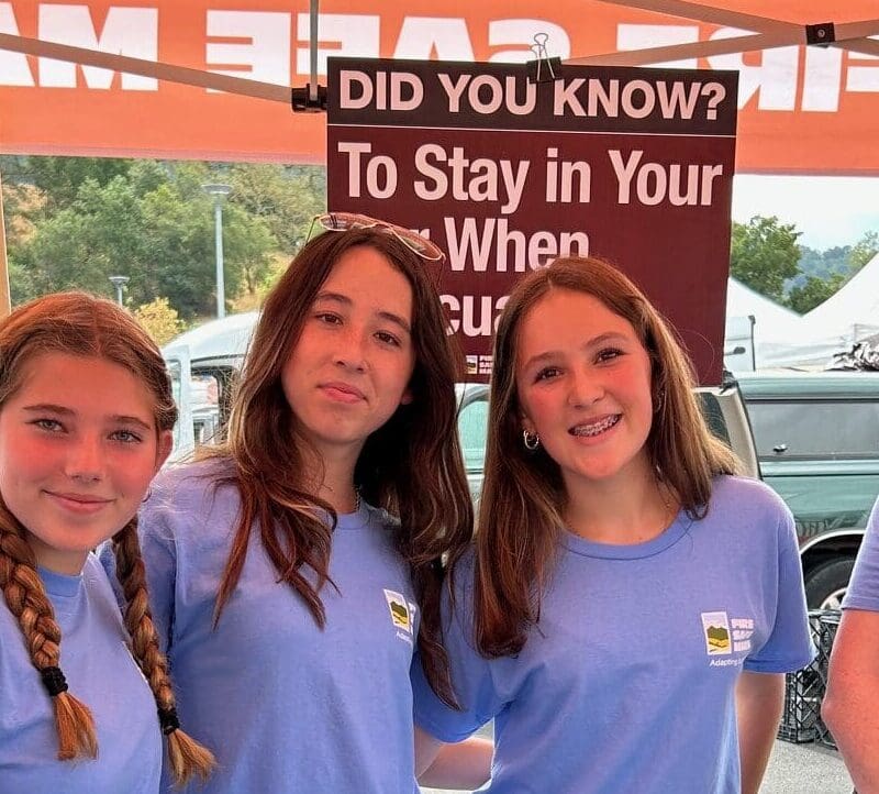 High school students volunteering at farmers market, standing at a booth for fire safety program.