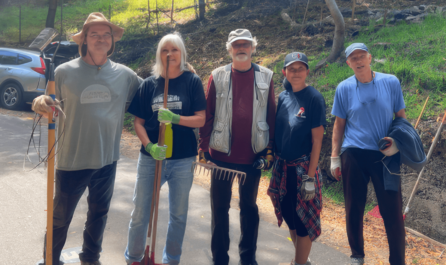 group of people smiling for the camera holding gardening tools