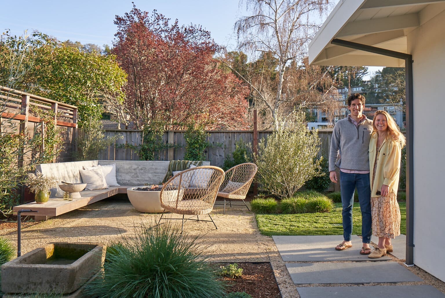 A young couple stand next to their outdoor seating area in their back yard.