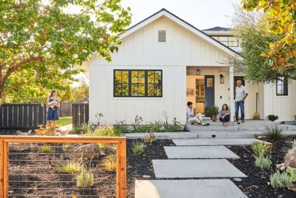 A single story house with a drought tolerant garden. A family of 4 are on the porch, relaxing.