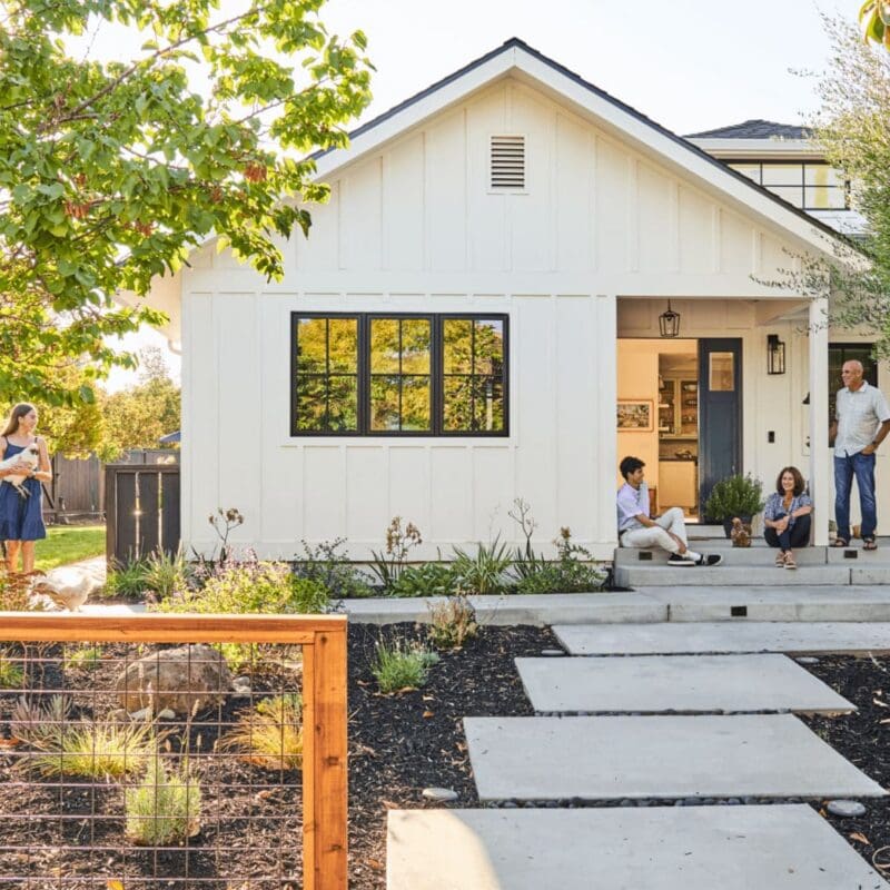 A single story house with a drought tolerant garden. A family of 4 are on the porch, relaxing.