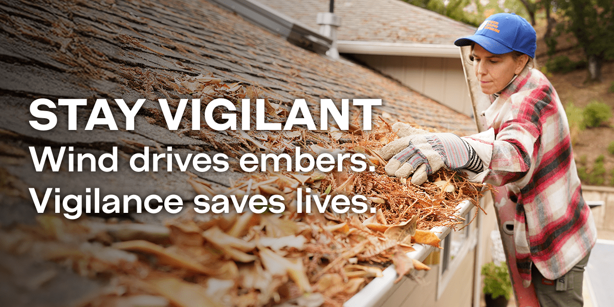 Woman clean leaves from roff gutters. "Stay Vigilant. Wind Drives embers. Vigilance saves lives"